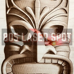 May include: A wooden tiki mask with intricate carvings and a stylized face. The mask has a large mouth with teeth, a prominent nose, and eyes with a fierce expression. The top of the mask is decorated with a floral design.