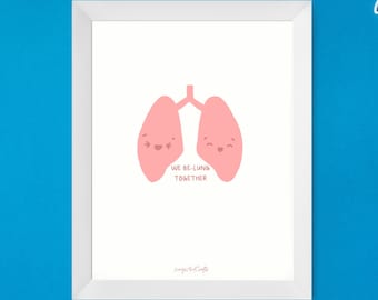 May include: A white framed print with a pink cartoon illustration of two lungs with smiling faces. The text "We be-lung together" is below the lungs. The print is hanging on a blue wall with two blue surgical masks on either side.
