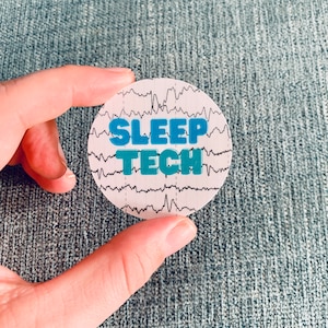 May include: A white round sticker with a black and white brainwave pattern and the text "SLEEP TECH" in blue letters.