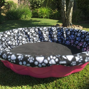 May include: A pink and black dog bed with a paw print design. The bed is made of a soft, plush material and is perfect for small to medium-sized dogs.