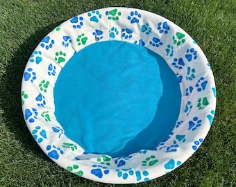Peut inclure: Un lit pour animal de compagnie blanc et bleu avec une doublure en polaire bleue et un motif de pattes.