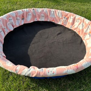 May include: A round, pink and white fabric-covered playpen with a black fabric bottom. The fabric has a pattern of white ghosts with black eyes and mouths.