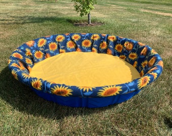 Peut inclure: Un lit pour animal de compagnie rond bleu et jaune avec un imprimé de tournesol. Le lit est doublé d'un tissu jaune.