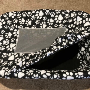 May include: Black and white pet bed with a paw print pattern. The bed has a mesh window and is partially open to show the black interior.