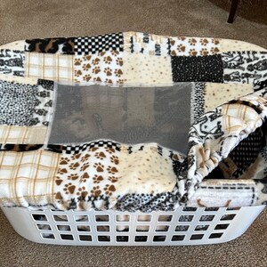 May include: A white plastic laundry basket with a brown, black, and white patchwork fabric liner. The liner has a mesh window and is folded over the top of the basket.