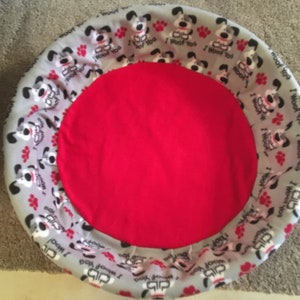 May include: A red dog bed with a gray and white patterned border. The border features a repeating pattern of a cartoon dog with the text "I woof you" and paw prints.