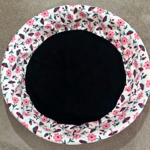 May include: A round, white fabric pet bed with a black center and a pink and green mushroom print.