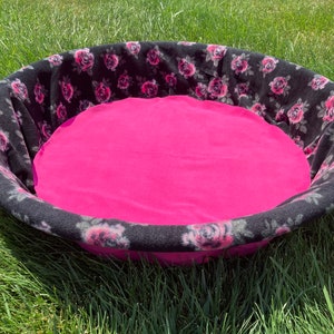 May include: A black and pink pet bed with a floral print. The bed is round and has a soft, plush lining.