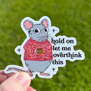May include: A sticker featuring a cartoon mouse wearing a pink sweater and holding a cup of coffee. The text on the sticker reads "hold on let me overthink this".