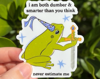Può includere: Un adesivo fustellato raffigurante una rana verde che indossa un cappello da mago blu con stelle, che impugna una spada con una gemma blu. Il testo recita: i am both dumber & smarter than you think e never estimate me, circondato da icone di stelle blu.