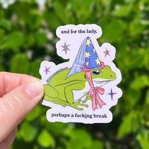 Pu&ograve; includere: Un adesivo a forma di rana verde con un cappello da mago con stelle blu e gialle e un fiocco rosa. L'adesivo ha il testo "and for the lady, perhaps a fucking break". L'adesivo &egrave; tenuto in mano.