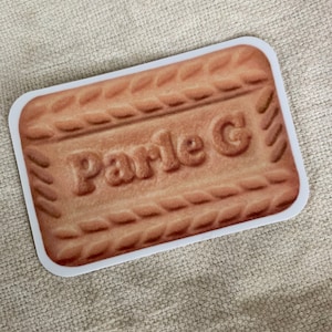 May include: A rectangular sticker depicting a Parle-G biscuit. The biscuit is light brown with the embossed text "Parle G". The sticker has a white border and is set against a neutral background.