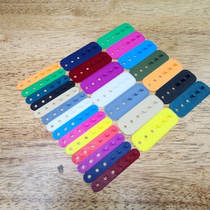 May include: A set of 18 colorful plastic rectangular buttons with five holes each. The buttons are arranged in a fan shape, with the colors ranging from red, orange, yellow, green, blue, purple, and white.