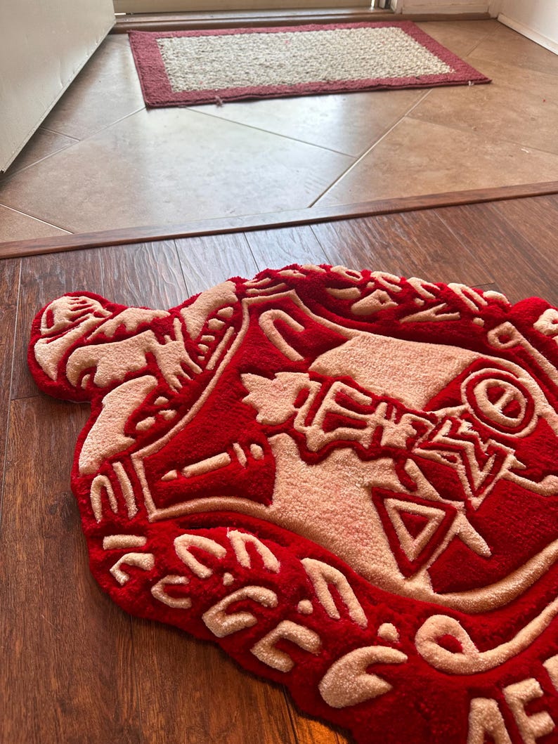 Puede incluir: Una alfombra roja y beige con una forma y dise&ntilde;o &uacute;nicos. La alfombra presenta un fondo rojo intenso con detalles beige, creando un contraste llamativo. El dise&ntilde;o incluye formas y patrones abstractos, agregando un toque moderno al revestimiento del suelo.