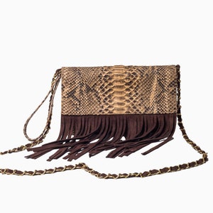 Op de afbeelding: Een bruine clutch van slangenleer met een franje detail en een gouden kettingriem.