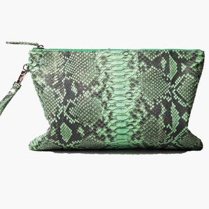 Op de afbeelding: Een groene slangenleren clutch met een zwarte band.