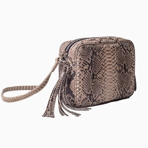 Może przedstawiać: Kwadratowa torba na ramię z wzorem skóry węża w odcieniach brązu i szarości. Posiada zapięcie na zamek błyskawiczny, mały uchwyt i ozdobny chwost. Torba jest przeznaczona do przenoszenia niezbędnych przedmiotów.