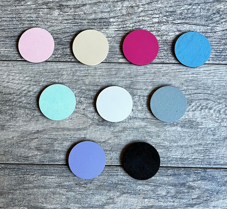 Puede incluir: Diez discos redondos de madera en varios colores, incluyendo rosa, beige, rojo, azul, azul claro, blanco, gris, morado y negro. Los discos est&aacute;n dispuestos en semic&iacute;rculo sobre una superficie de madera.