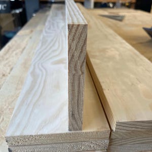 May include: Close-up of the edge of a wooden plank, showing the layers of wood that make up the plank. The wood is light brown in colour and has a smooth finish.