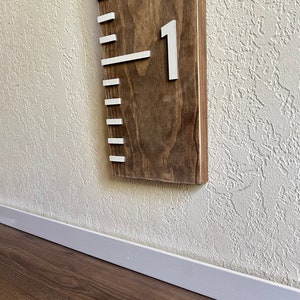 May include: A wooden growth chart with white markings and the number "1" on it. The chart is mounted on a white wall.