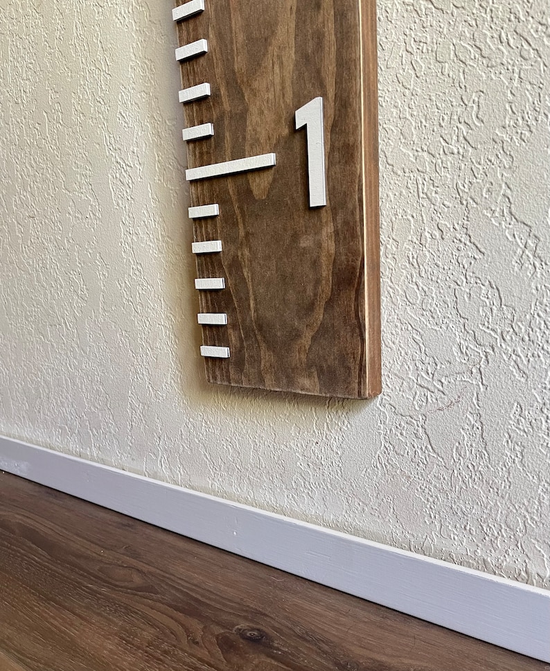 May include: A wooden growth chart with white markings and the number "1" on it. The chart is mounted on a white wall.
