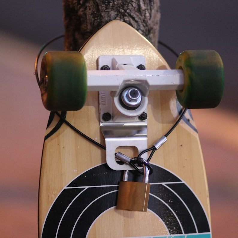 Puede incluir: Una tabla de skate de madera con rayas blancas y negras, ruedas verdes y un candado de metal plateado sujeto a la plataforma.