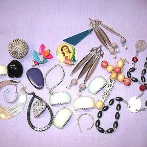 May include: A collection of vintage jewelry pieces, including earrings, necklaces, and brooches, arranged on a lavender surface. The jewelry features various shapes, colors, and materials, such as silver, beads, and gemstones. Some pieces have a retro aesthetic.