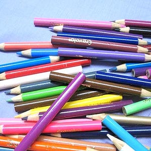 May include: A collection of Crayola colored pencils in various colors, including pink, blue, green, and brown. The pencils are scattered on a light blue surface, with some pencils displaying the Crayola brand name.