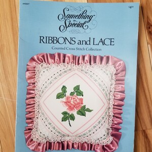 May include: A counted cross stitch pattern booklet titled "Ribbons and Lace" by Something Special. The cover features a pink satin cushion with a white lace trim and a cross stitch design of a pink rose.