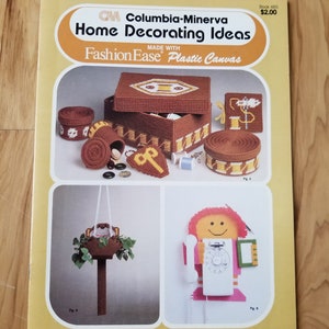 May include: A book cover for a craft project book titled "Columbia-Minerva Home Decorating Ideas" made with Fashion Ease Plastic Canvas. The cover features a variety of plastic canvas projects, including a box, a hanging planter, and a phone holder.