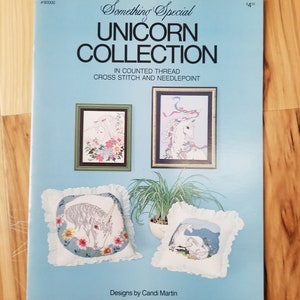 May include: A blue and white booklet with the title "Something Special Unicorn Collection" in counted thread cross stitch and needlepoint. The booklet features four images of unicorns, two in frames and two on pillows. The text "Designs by Candi Martin" is at the bottom of the page.
