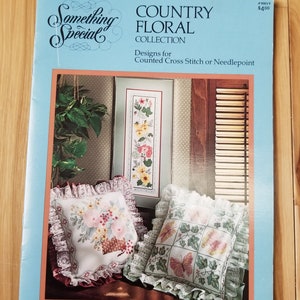 May include: A light blue book cover with the title "Something Special COUNTRY FLORAL COLLECTION" featuring cross-stitch designs. The cover displays floral cross-stitch patterns on pillows and a framed piece. Designs by Candi Martin.