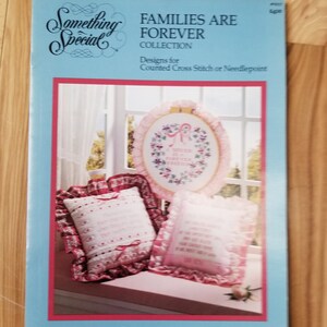 May include: A blue and white booklet with the title "Something Special Families Are Forever Collection" and the text "Designs for Counted Cross Stitch or Needlepoint" on the front cover. The booklet features a pink and white cushion with a floral design and the text "Families Are Forever" in the centre. The booklet also features a pink and white cushion with the text "Our Family Is A Circle Of Strength And Love" in the centre.