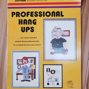 May include: A yellow and purple leaflet with the title "Professional Hang Ups" and a subtitle "...are career minded people done professionally in counted thread cross stitch!" The leaflet features three cross stitch patterns: a doctor, a lawyer, and a nurse.