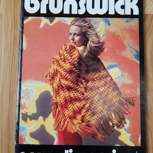 May include: A magazine cover featuring a woman wearing a colourful crocheted shawl with fringe. The magazine is titled "Brunswick" and the text "new dimensions" is printed at the bottom. The cover features a bright orange, yellow, and red background.