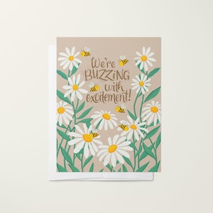 May include: A greeting card with a beige background featuring white daisies and yellow bees. The text on the card reads "We're buzzing with excitement!"