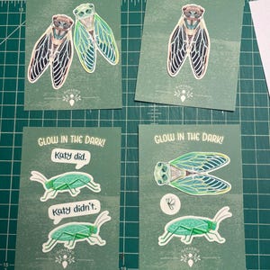 Puede incluir: Tarjetas verdes con ilustraciones de insectos y el texto "GLOW IN THE DARK!". Algunas tarjetas presentan cigarras, otras saltamontes con bocadillos que dicen "Katy did" y "Katy didn't".