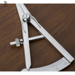 May include: A silver metal compass with a protractor scale marked in increments of 5 up to 20. The compass has a screw adjustment for setting the radius.