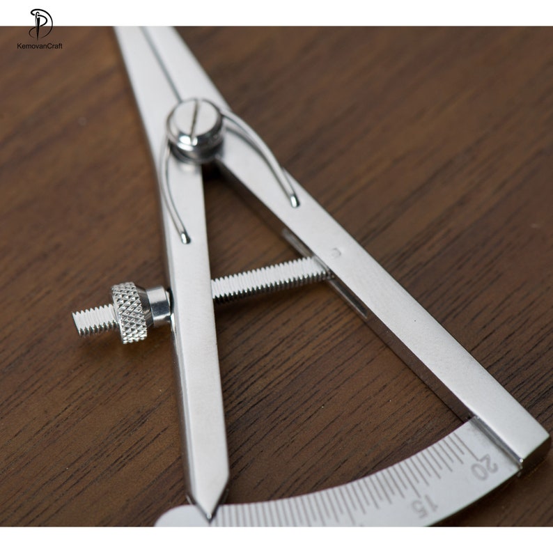 May include: A silver metal compass with a protractor scale marked in increments of 5 up to 20. The compass has a screw adjustment for setting the radius.