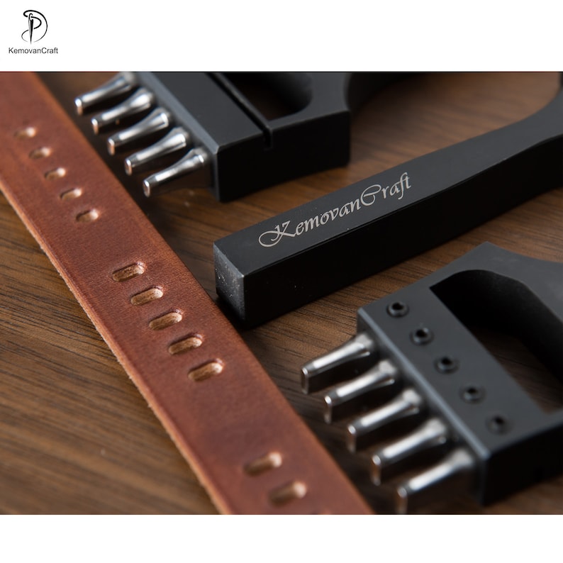 May include: Close-up of leather crafting tools and a brown leather strap. The tools are black with silver metal components. The text "KemovanCraft" is engraved on one of the tools. The leather strap has evenly spaced holes.