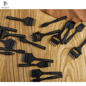 May include: A collection of black leathercraft tools, including various sizes of pronged chisels and punches. The tools are arranged on a wooden surface, showcasing their different widths and prong configurations. The brand name "KemovanCraft" is visible on each tool.