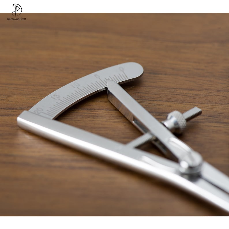 May include: A silver metal compass with a graduated protractor. The compass is open and the protractor is set to 20 degrees.
