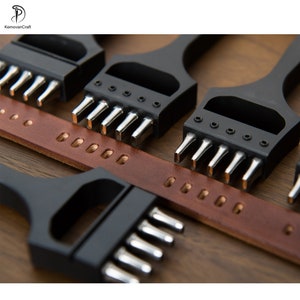 May include: Close-up of leatherworking tools, including black metal hole punches with silver teeth, and a brown leather strap with punched holes. The tools are arranged on a wooden surface, showcasing the craft.
