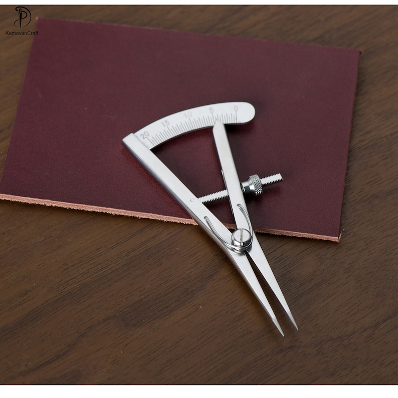 May include: A silver leather crafting tool with a graduated protractor and adjustable arms. The tool is used to measure and mark leather for cutting and stitching.