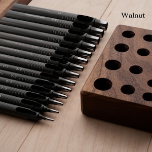 May include: A set of black leathercraft hole punches with varying sizes, labeled with measurements, and a walnut wood holder. The text "KenovanCraft" is printed on the punches. The holder has multiple circular holes for storage. The word "Walnut" is printed on the image.