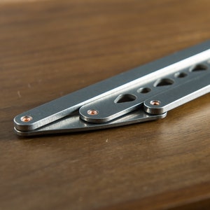 May include: A silver folding knife with a textured handle and copper-colored rivets. The knife is partially open, revealing the blade.