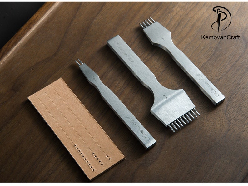 May include: A set of silver leather working tools, including stitching chisels and a leather sample with pre-punched holes. The tools are arranged on a wooden surface, showcasing the craftsmanship of leatherwork.