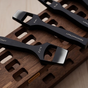 May include: A set of black leatherworking tools with angled blades, arranged on a wooden holder. The tools are marked with measurements and the brand name "KEMOVANCRAFT". The wooden holder has a geometric design.