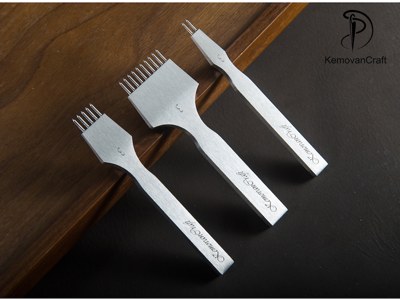 May include: Three silver leathercraft tools with multiple prongs, arranged on a dark surface. The tools have a handle and a numbered marking. The text "KemovanCraft" is printed on the handle of each tool.