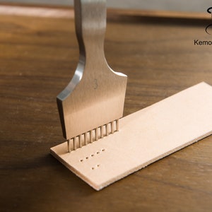 May include: A metal leathercraft tool with multiple prongs is pressed into a strip of light tan leather. The tool is marked with the number "3". The logo "KemovanCraft" is visible in the upper right corner. The leather strip is on a wooden surface.